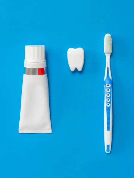 A tooth figurine, a tube of toothpaste and a blue toothbrush with silicone bristles on a blue background. Flat lay. — Stock Photo, Image