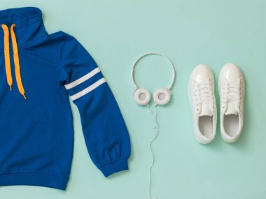 Beyaz spor ayakkabılar, beyaz spor ayakkabılar ve mavi arka planda beyaz çizgili bir sweatshirt..