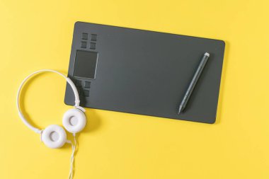 Sarı arka planda grafik tabletinin yanında kablo olan beyaz kulaklıklar..