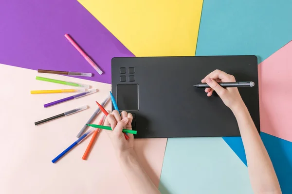 Handen met een set gekleurde markers en een grafische tablet op een veelkleurige papieren achtergrond. — Stockfoto