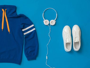 Spor kıyafetleri ve parlak mavi arka planda kulaklıklı ayakkabılar..