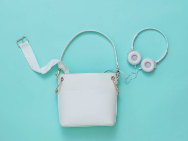 Kemerli deri kadın çantası ve açık mavi arka planda beyaz kulaklıklar. Düz yatıyordu.