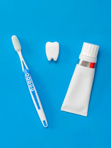 Figure of a tooth between a toothpaste and a brush on a blue background. Flat lay. — Stock Photo, Image