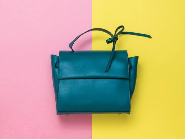 Sarı ve kırmızı arka planda deri bağcıklı koyu turkuaz kadın çantası. Yukarıdan görünüşü.