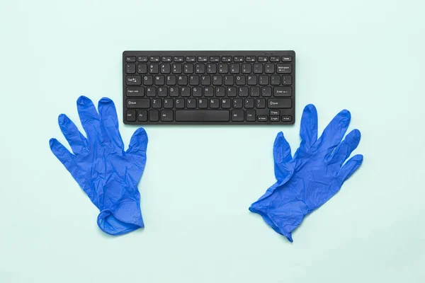 Keyboard and blue medical gloves on a light background.