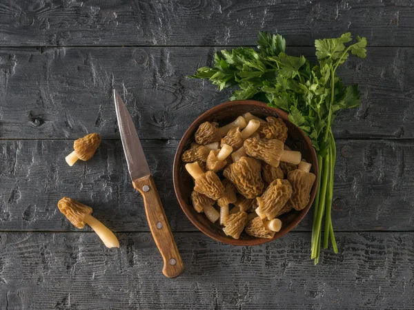 A knife and parsley leaves next to a bowl of morels. — Stock Photo, Image