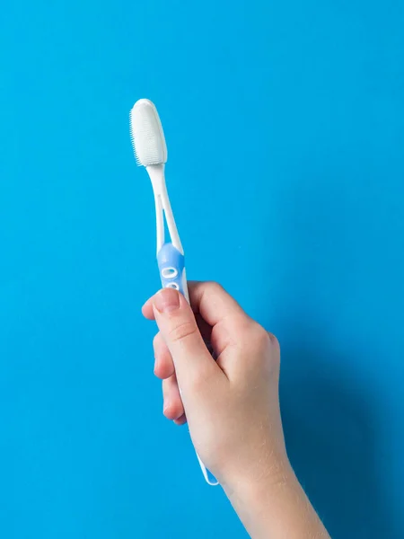 A child's hand with a blue toothbrush on a blue background. — Stock Photo, Image