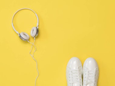 Şık beyaz spor ayakkabılar ve parlak sarı bir arka planı olan beyaz kulaklıklar..
