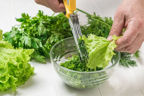 Um homem corta ervas frescas em uma saladeira de vidro . — Fotografia de Stock