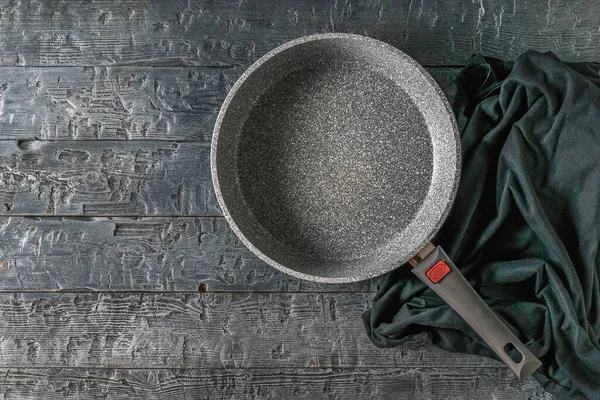 Una sartén profunda y un trozo de tela sobre una mesa de madera negra . — Foto de Stock