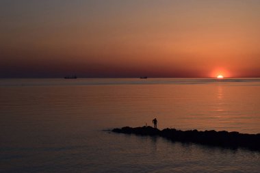 Karadeniz kıyısından gün batımının manzarası. İnsan balık yakalar. Gemiler denizde yelken açıyor..