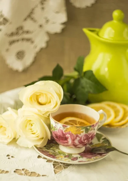 Чашка чая с лимоном и белыми розами на вышитой салфетке — стоковое фото