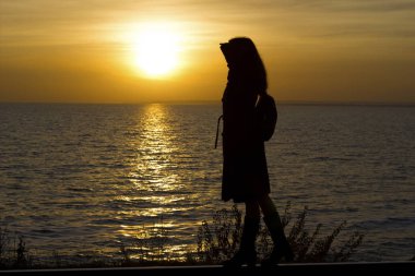 Kız gün batımında paltosuyla tren yolunda yürüyor.