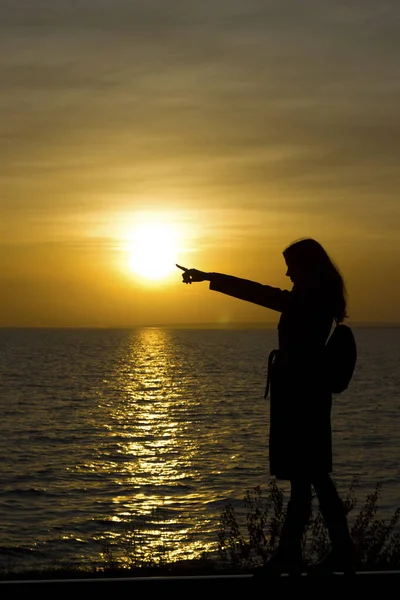 Girl walks on railroad tracks in coat indicate, point on sunset background — Stock Photo, Image