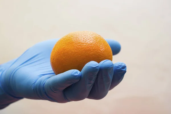 Hand in a medical glove holds an orange - vitamin for immunity instead of pills, coronavirus, covid19