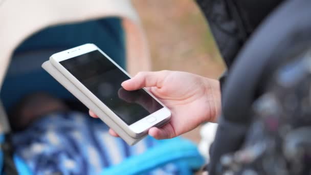 Girl typing on her smart phone on baby in pram background — Stockvideo