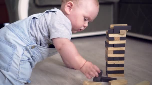 Baby boy destroing jenga tower with wooden building boards — ストック動画