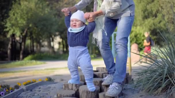 Das Kind macht die ersten Schritte, die Mutter hilft ihm. Herbstpark. — Stockvideo