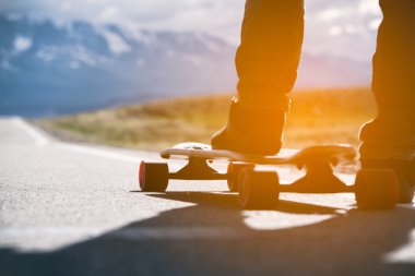 Dağlarda yolda longboard sporcu ayağı olduğunu. Güneş ışığı.