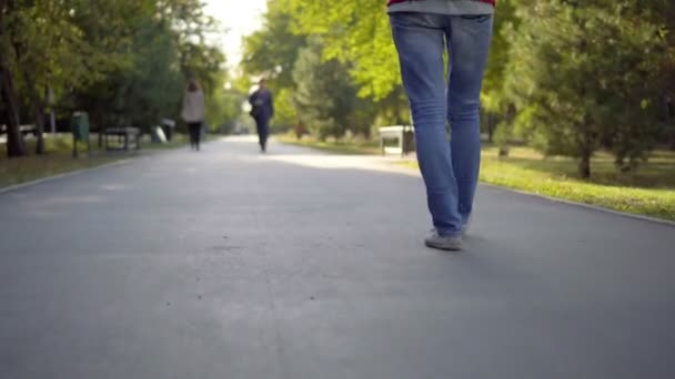 Een vrouw in spijkerbroek wandelen in het park. Asfalt. — Stockvideo