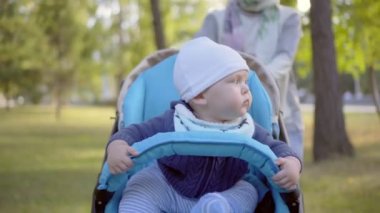 Anne, bir bebek arabası için yürümeye başlayan çocuk alır. Gülümseyen ve etrafa bebeğim. Açık.