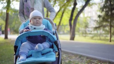 Anne, bir bebek arabası için yürümeye başlayan çocuk alır. Kollarını sallayarak bebek. Açık.