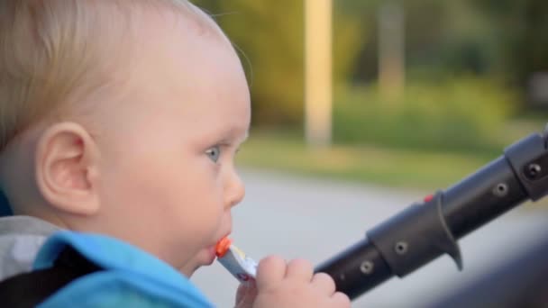 Bebê sentado em um carrinho de bebê e comendo um saco com comida de bebê . — Vídeo de Stock