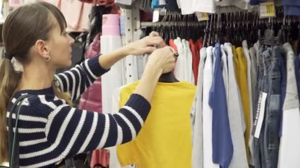 Young mother shopping for childrens clothes in a retail clothing store. Viewing items. — Stock Video