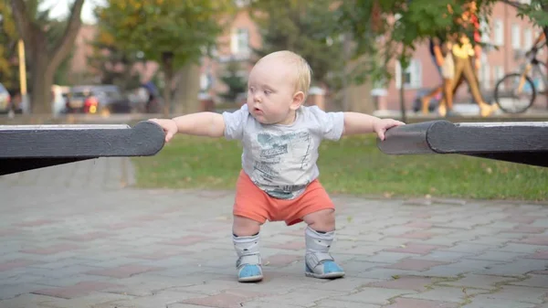 Der kleine Junge lernt, an der Bank entlang zu gehen. im Park. Außenbereich. — Stockfoto