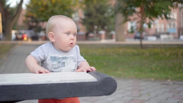 Little baby boy learns to walk along the bench. In the park. Outdoor. — Stock Video