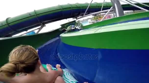 Счастливые мужчина и женщина скачут по водной горке. Развлекающиеся в аквапарке на курорте во время летних каникул — стоковое видео