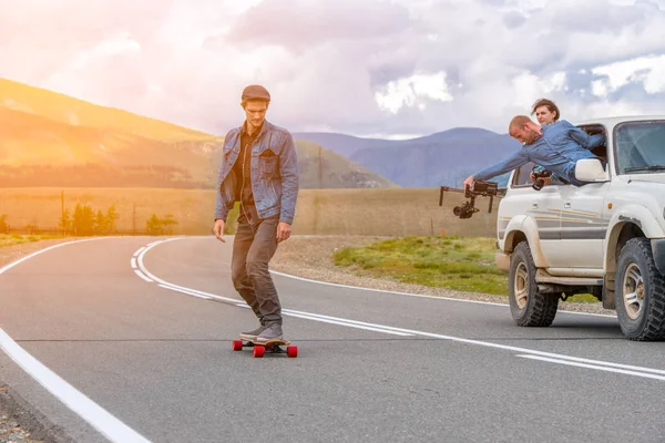 Adam ile dağlarda bir longboard gidiyor. Suv Araba sürme kameraman. O bir elektronik steadycam ile pencereden dışarı alır.