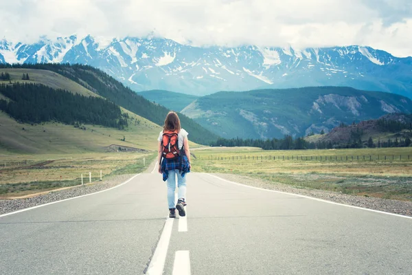 Einsames Mädchen mit Rucksack, das die Straße entlang läuft. in der Ferne, Berge. altai, russland. lizenzfreie Stockfotos