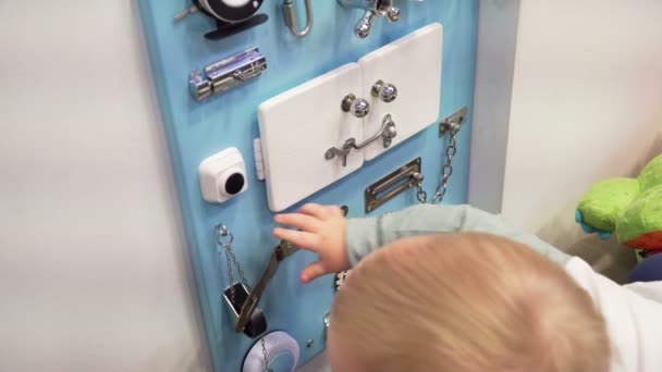 Baby jongetje aandachtig spelen met drukke bord aan de muur. Close-up. — Stockvideo