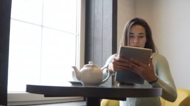 Genç esmer kız yakın pencere ve tablet pc içine bakmak masada oturur