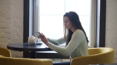 Genç esmer kız yakın pencere ve tablet pc içine bakmak masada oturur