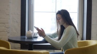 Genç esmer kız yakın pencere ve tablet pc içine bakmak masada oturur