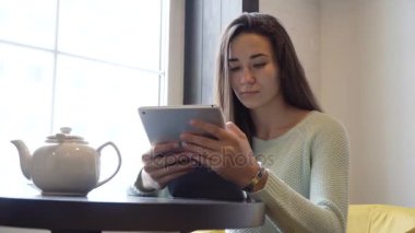 Genç esmer kız yakın pencere ve tablet PC'de masada oturur