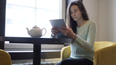 Genç esmer kız yakın pencere ve tablet PC'de masada oturur