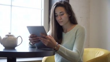 Genç esmer kız yakın pencere ve tablet PC'de masada oturur