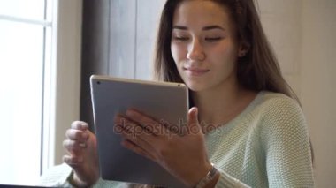 Genç esmer kız yakın pencere ve tablet PC'de masada oturur