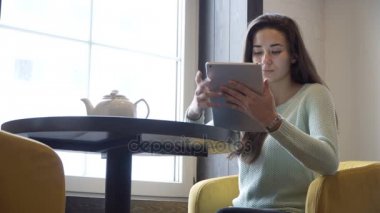 Genç esmer kız yakın pencere ve tablet PC'de masada oturur