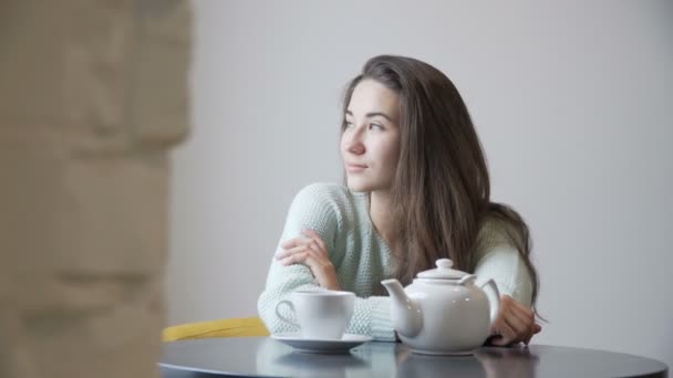 Flicka brunett sitter på ett café och tittar ut genom fönstret. — Stockvideo