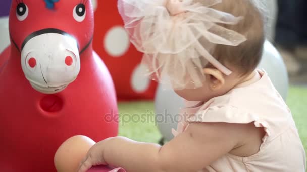 Маленькая девочка с большим бантиком играет с куклой. Рядом с игрушечным конём . — стоковое видео