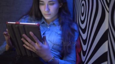 Tablet pc ile bir kanepede oturan genç güzel kız. Bir zebra gibi duvara. Çok renkli ışık. Kamera yavaş yavaş hareket eder. Elektronik Steadicam.