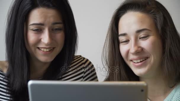 Two beautiful girls sitting in cafe, looking a tablet PC and laugh. Close-up. — Stock Video