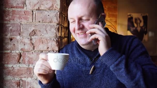 Man standing near a window in a cafe and drink coffee or tea, breakfast in restaurant. Talking on the phone. Wildly laughing. — Stock Video