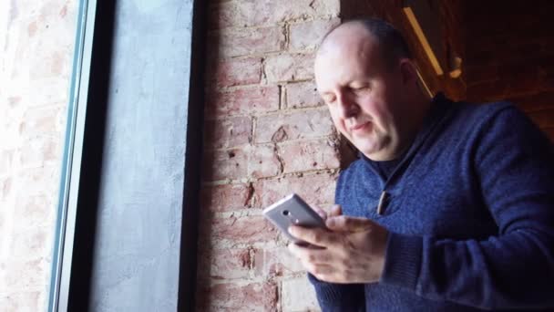 Ο άνθρωπος στέκεται κοντά σε ένα παράθυρο σε μια καφετέρια και χρησιμοποιώντας το smartphone, το πρωινό στο εστιατόριο. Γελώντας άγρια. — Αρχείο Βίντεο