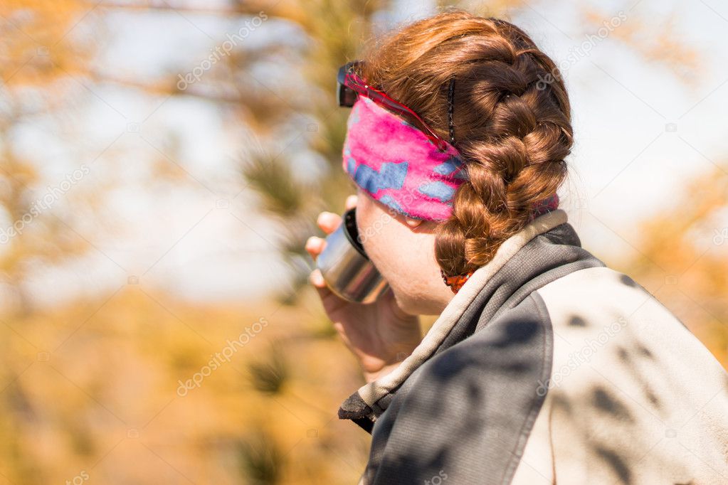 redhead girl drinks tea from a thermos in autumn in the mountain