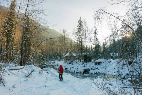 Donna con zaino passeggiate lungo il fiume di montagna nella neve — Foto Stock